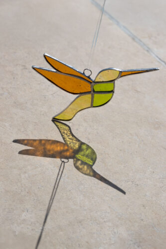 Colorful handmade stained glass hummingbird window suncatcher catching sunlight, home decoration