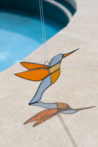 Colorful handmade stained glass hummingbird window suncatcher catching sunlight, home decoration