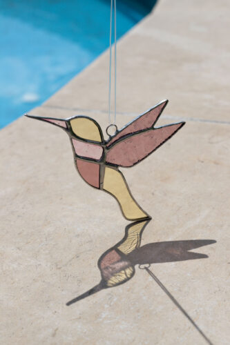 Colorful handmade stained glass hummingbird window suncatcher catching sunlight, home decoration