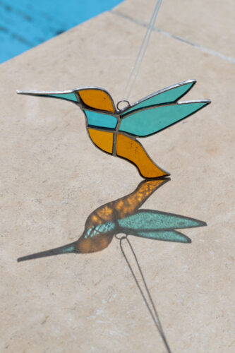 Colorful handmade stained glass hummingbird window suncatcher catching sunlight, home decoration