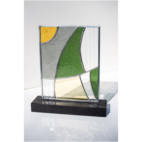 Abstract modern stained glass panel featuring textured and smooth glass elements, mounted on a minimalist wood block stand