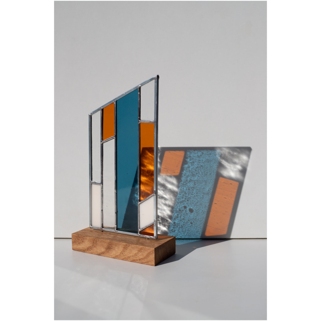 Abstract modern stained glass panel featuring textured and smooth glass elements, mounted on a minimalist wood block stand