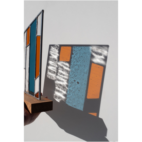Abstract modern stained glass panel featuring textured and smooth glass elements, mounted on a minimalist wood block stand
