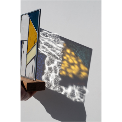 Abstract modern stained glass panel featuring textured and smooth glass elements, mounted on a minimalist wood block stand