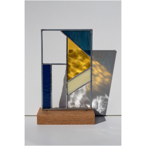 Abstract modern stained glass panel featuring textured and smooth glass elements, mounted on a minimalist wood block stand