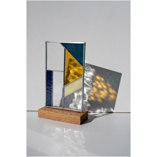 Abstract modern stained glass panel featuring textured and smooth glass elements, mounted on a minimalist wood block stand