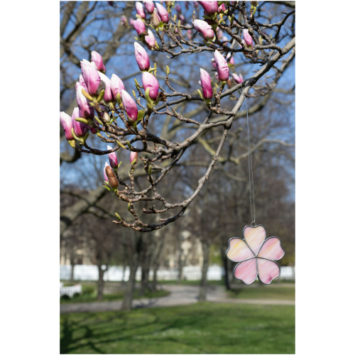 Handheld handcrafted Sakura cherry blossom suncatcher made of pink and yellow opalescent stained glass against a blurry spring tree background.